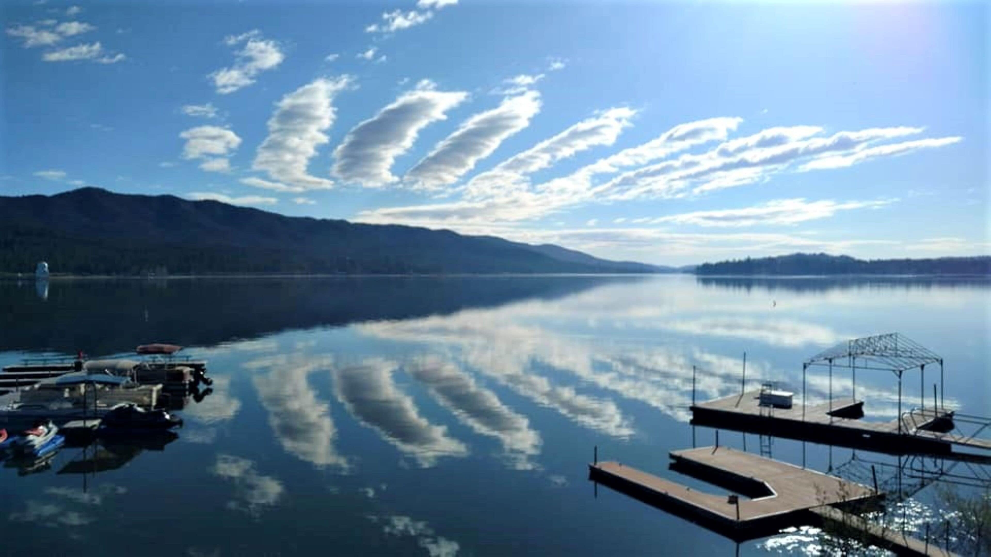 A calm lake with a dock and boats, surrounded by mountains and clear skies.