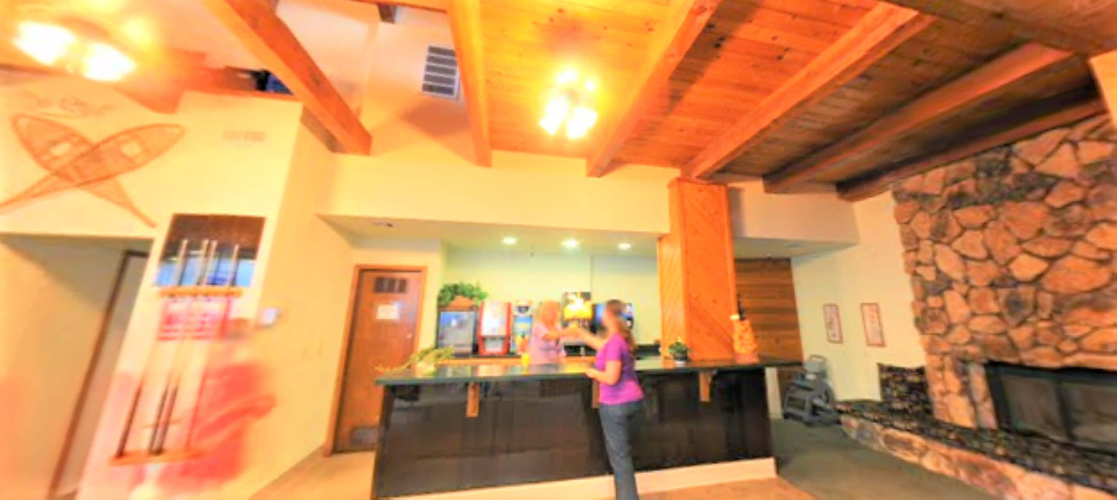 Un hall con mostrador de recepción, chimenea de piedra y vigas de madera en el techo.