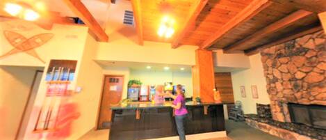 A lobby with a reception desk, a stone fireplace, and wooden ceiling beams.