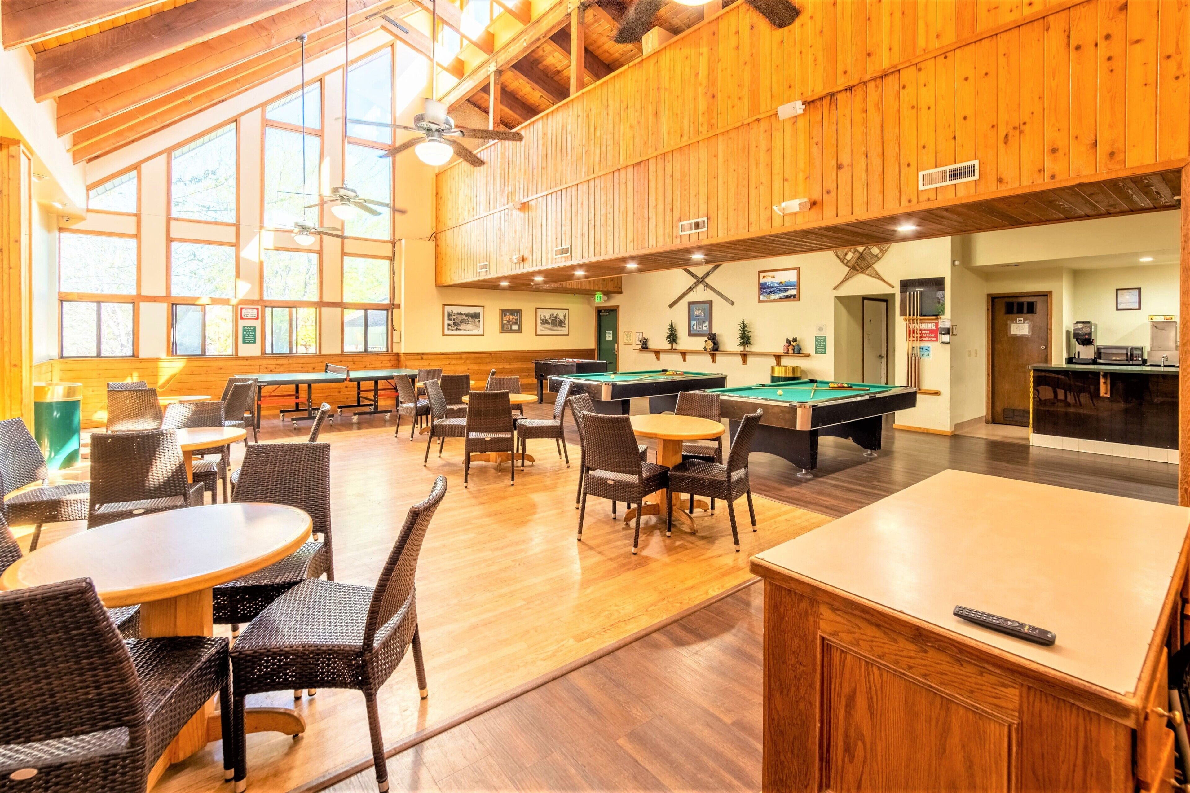 A spacious indoor area with wooden walls and ceiling, featuring a pool table, billiards, and multiple seating areas with tables and chairs.