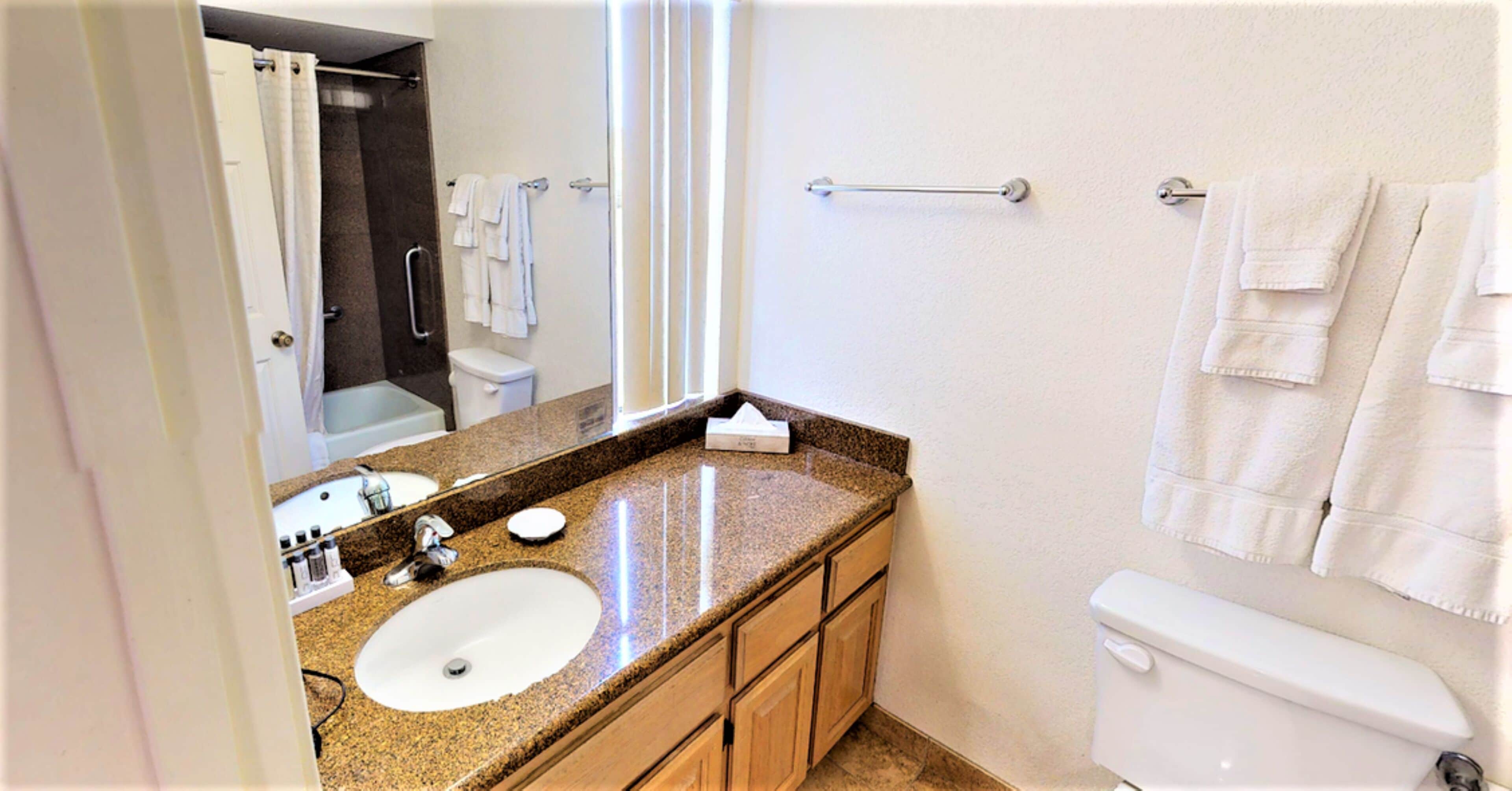 A bathroom with a granite countertop sink, wooden cabinets, a white toilet, and a towel rack.