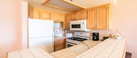 Una cocina con gabinetes de madera, un refrigerador blanco, un microondas, una estufa y una cafetera.