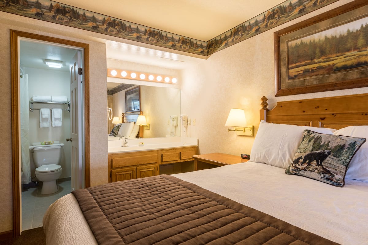 Een hotelkamer met een bed, een badkamer, een kaptafel met spiegel en een schilderij aan de muur.