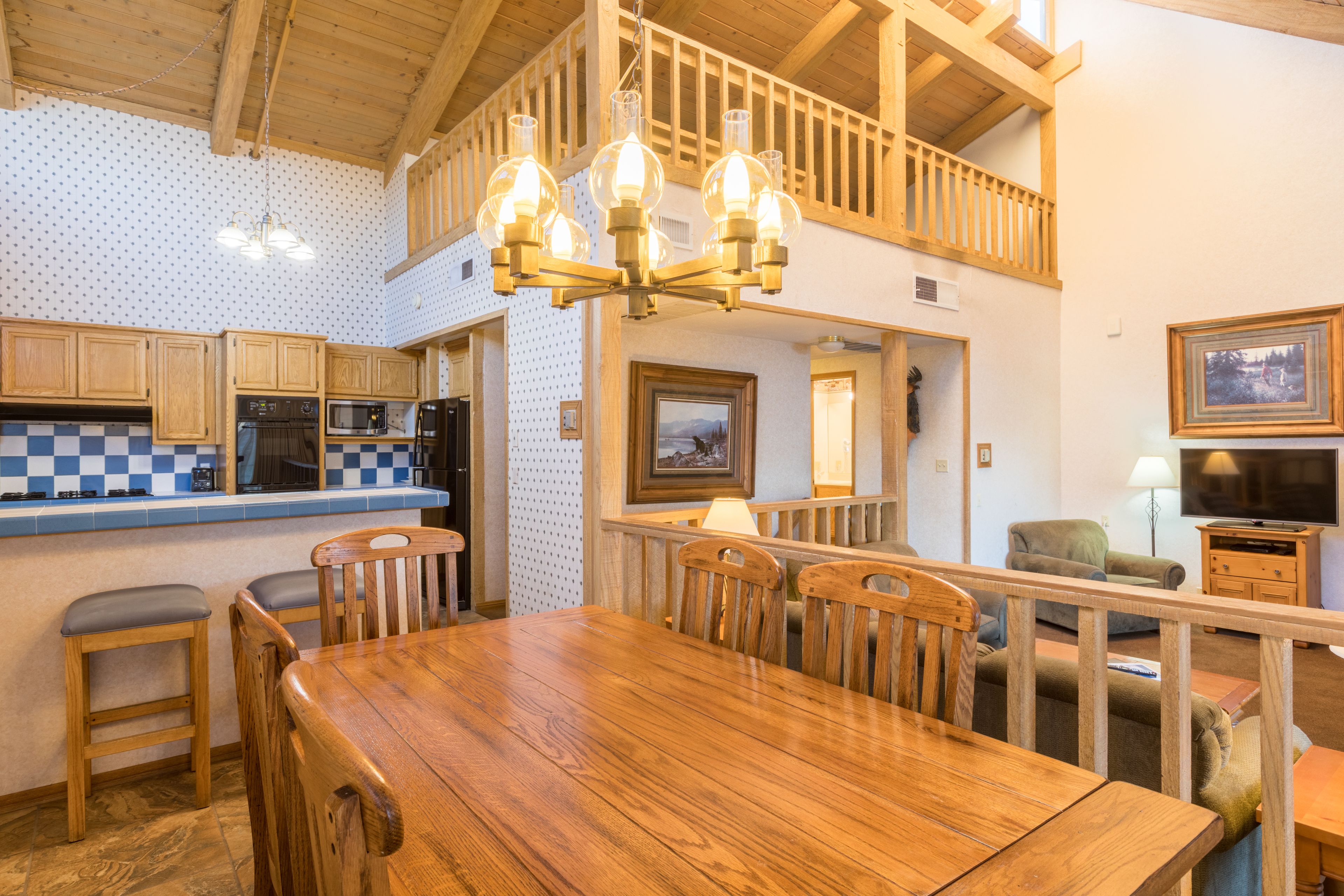Une table de salle à manger en bois avec des chaises, une cuisine équipée d’un four à micro-ondes et un balcon doté d’une balustrade en bois.