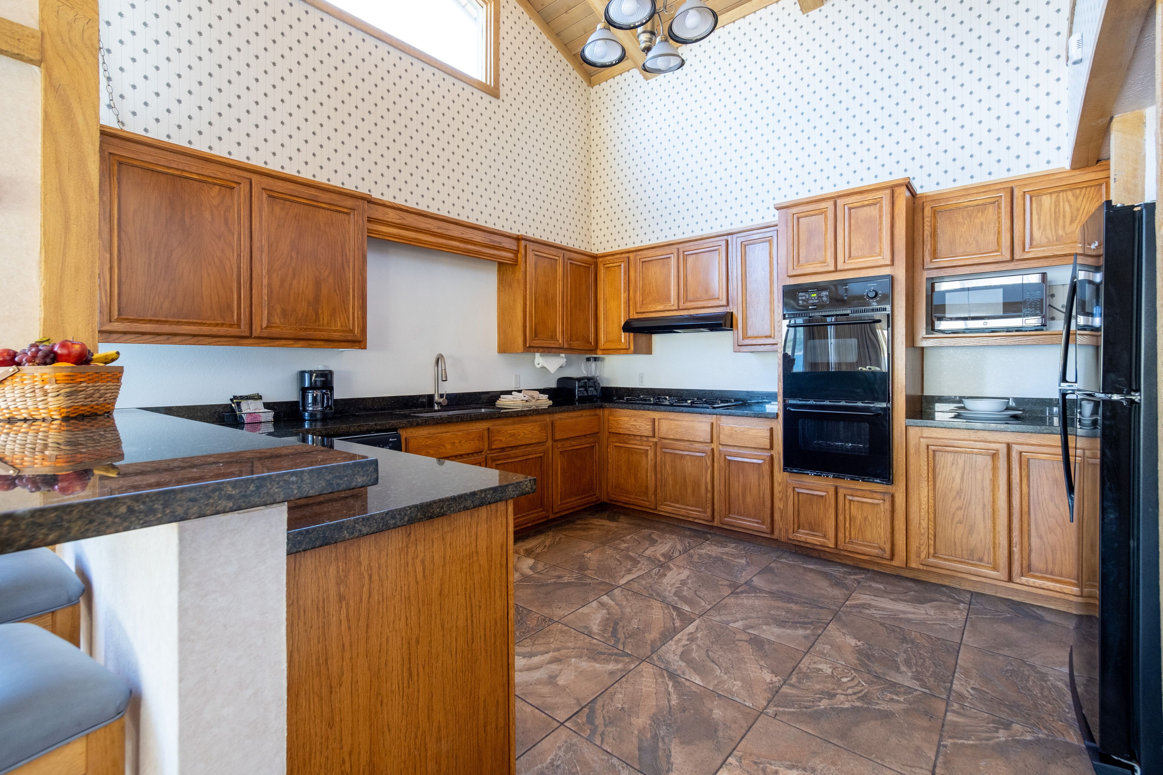 Una cocina con gabinetes de madera, encimera de granito, refrigerador negro y microondas.