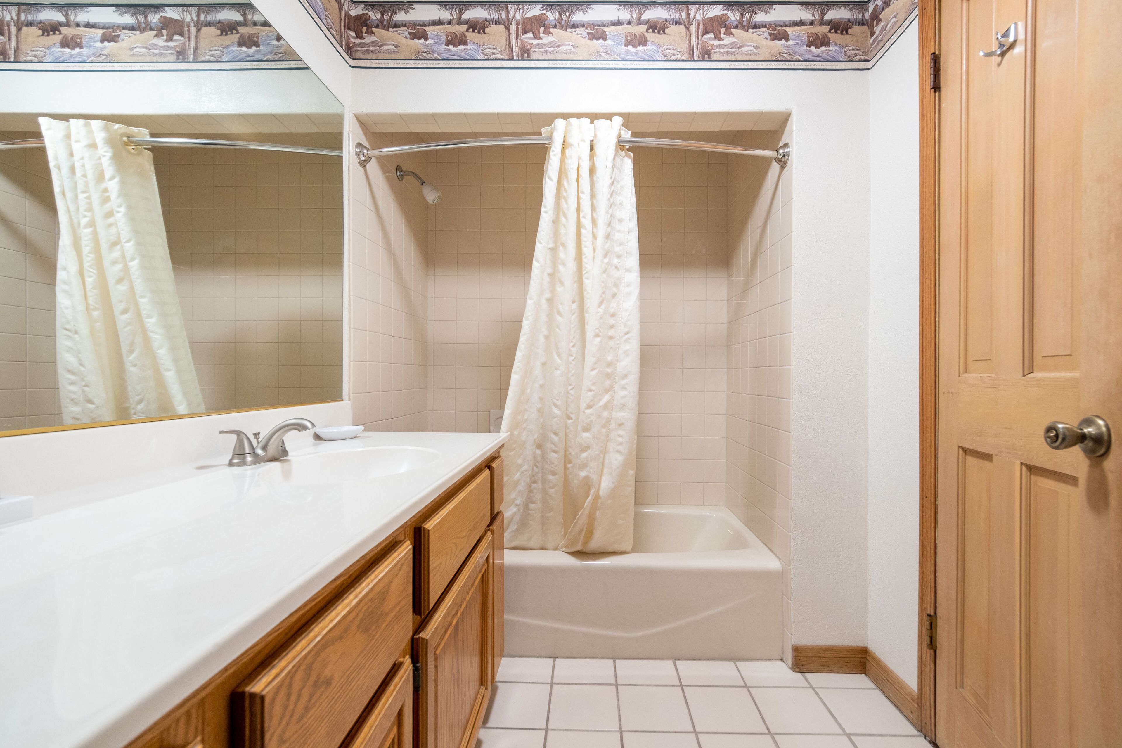 Une salle de bain avec un lavabo blanc, des meubles en bois, une baignoire et un rideau de douche.