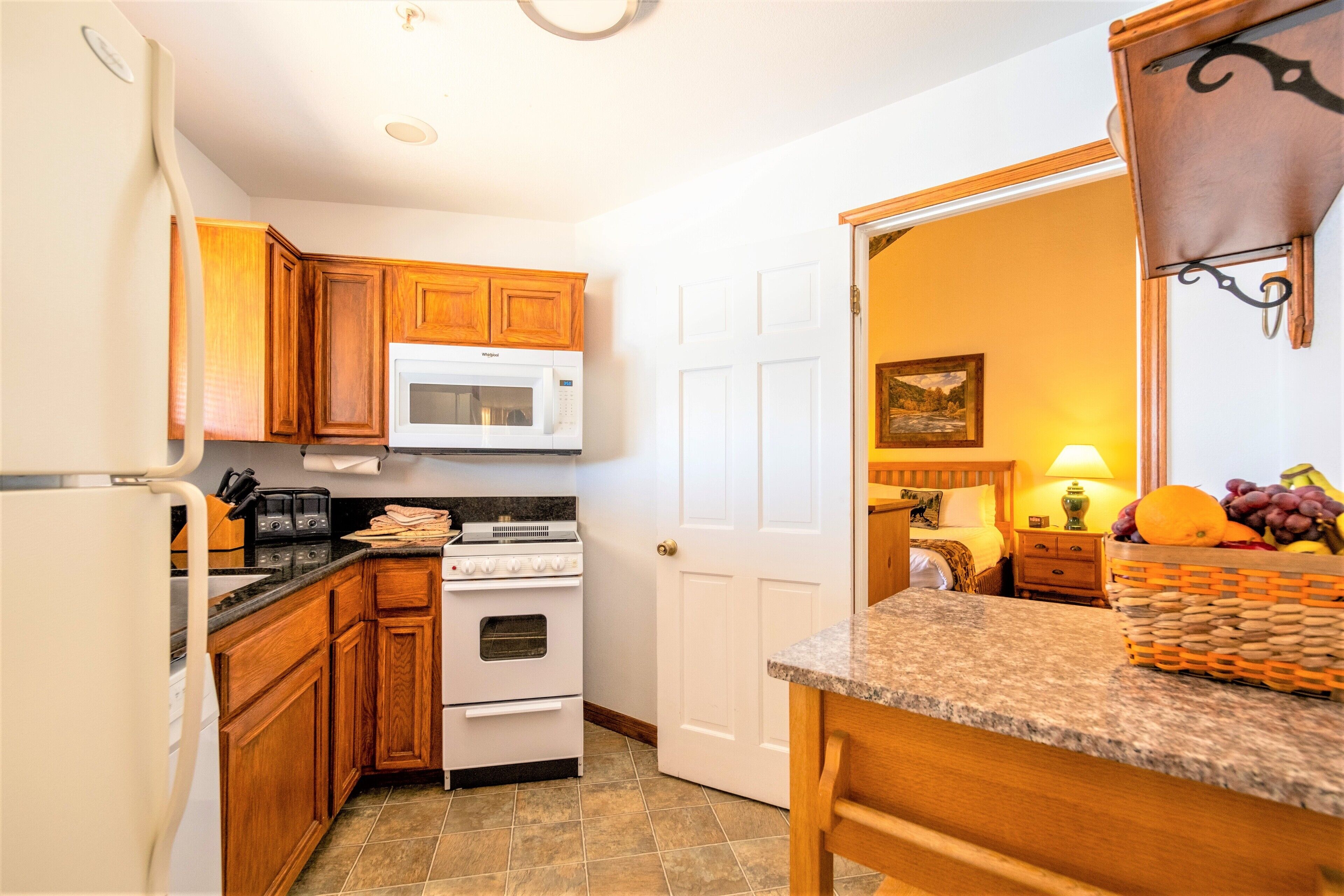 A kitchen with wooden cabinets, a white microwave, a stove, and a refrigerator.