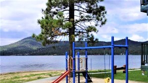A playground with a slide and swings, set against a lake and mountains. - Lagonita Lodge (Big Bear Lake)