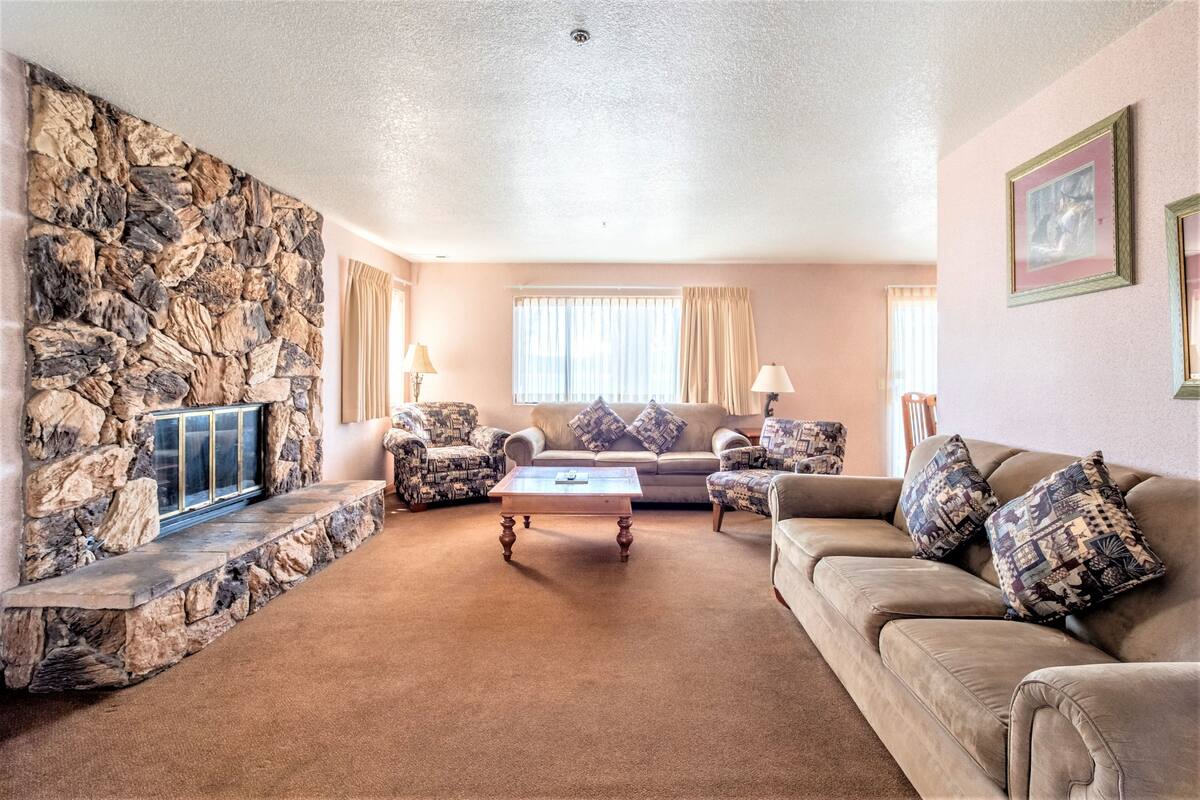 Een woonkamer met een stenen openhaard, een beige bank, een gestreept fauteuil en een salontafel.