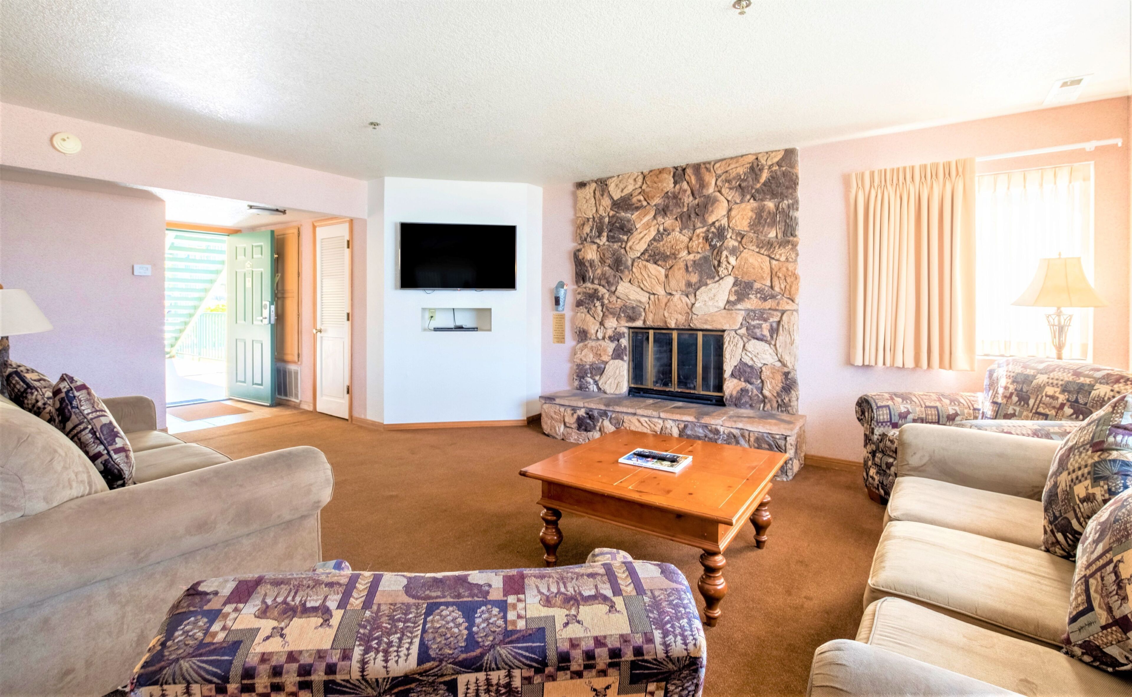 A living room with a stone fireplace, a flat-screen TV, and patterned furniture.