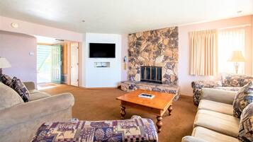 A living room with a stone fireplace, a flat-screen TV, and patterned furniture.
