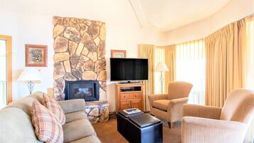 A living room with a stone fireplace, a flat-screen TV, a sofa, and two armchairs.