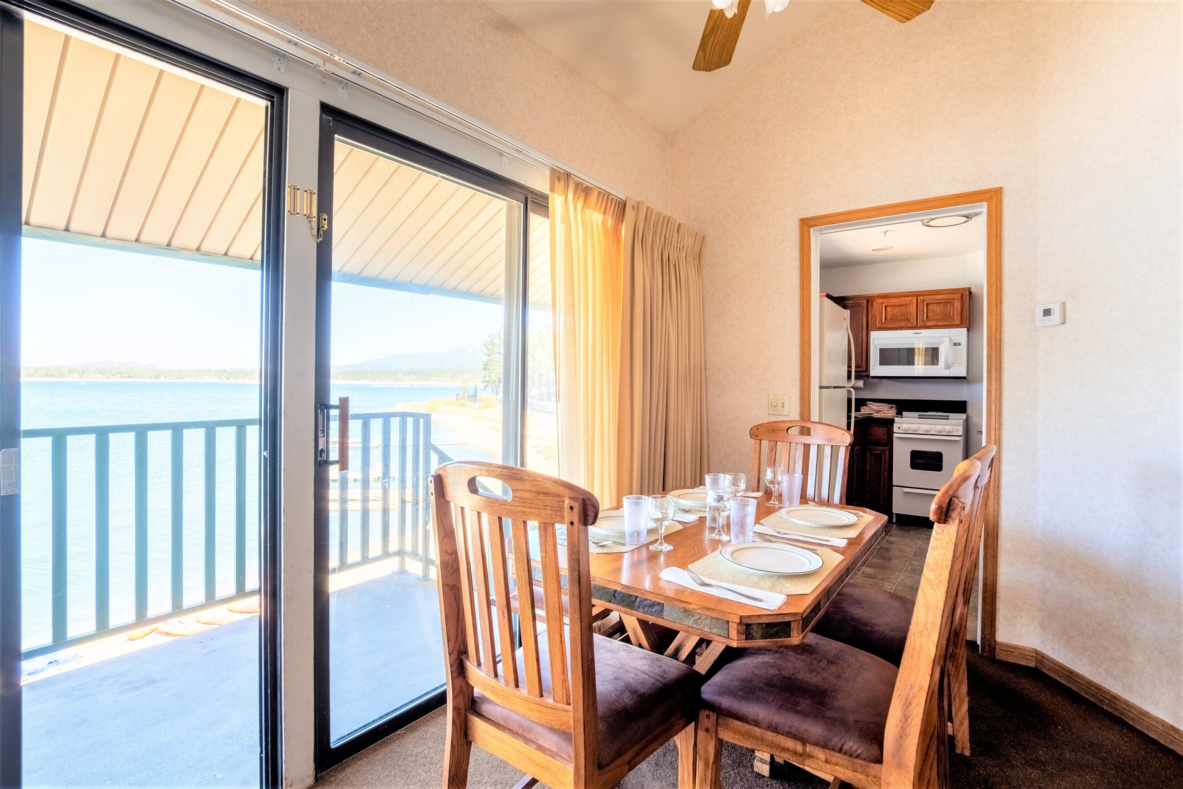 Un coin repas avec une table dressée pour quatre personnes, une porte-fenêtre coulissante donnant sur un balcon et une cuisine visible à travers une porte adjacente.