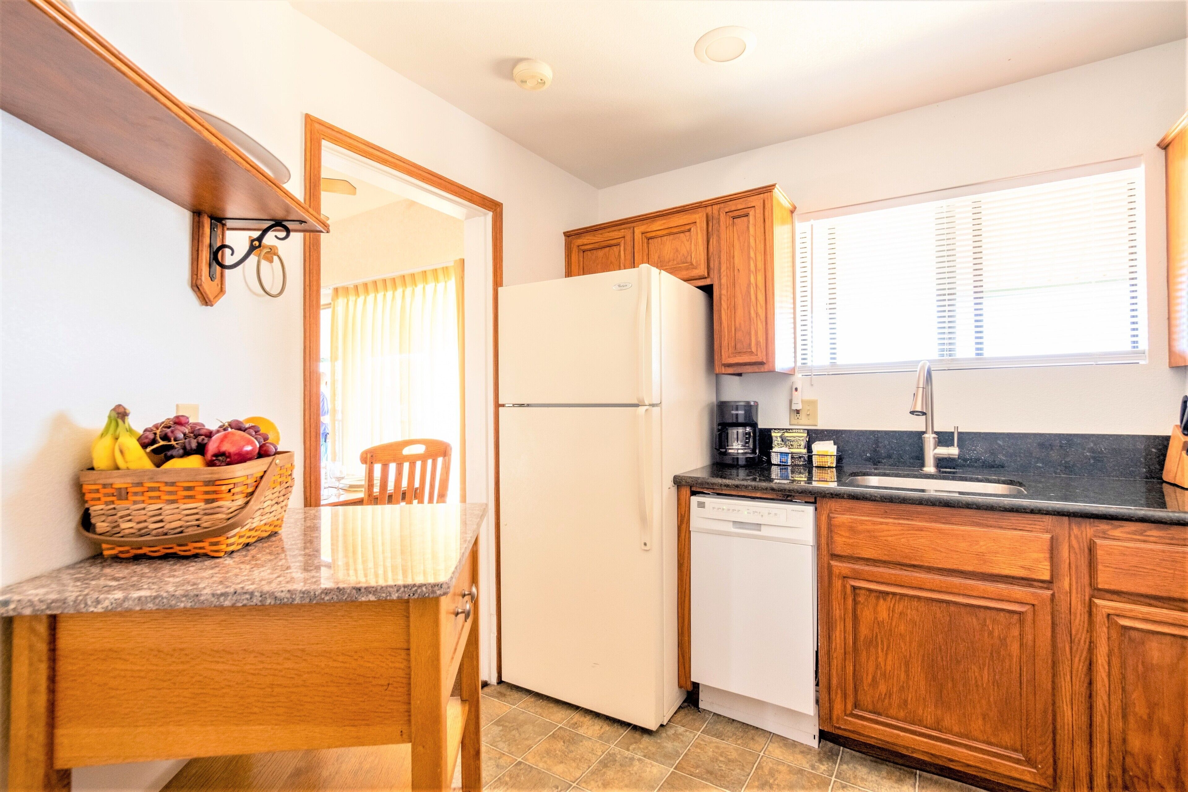 A kitchen with wooden cabinets, a white refrigerator, a granite countertop, and a basket of fruit.