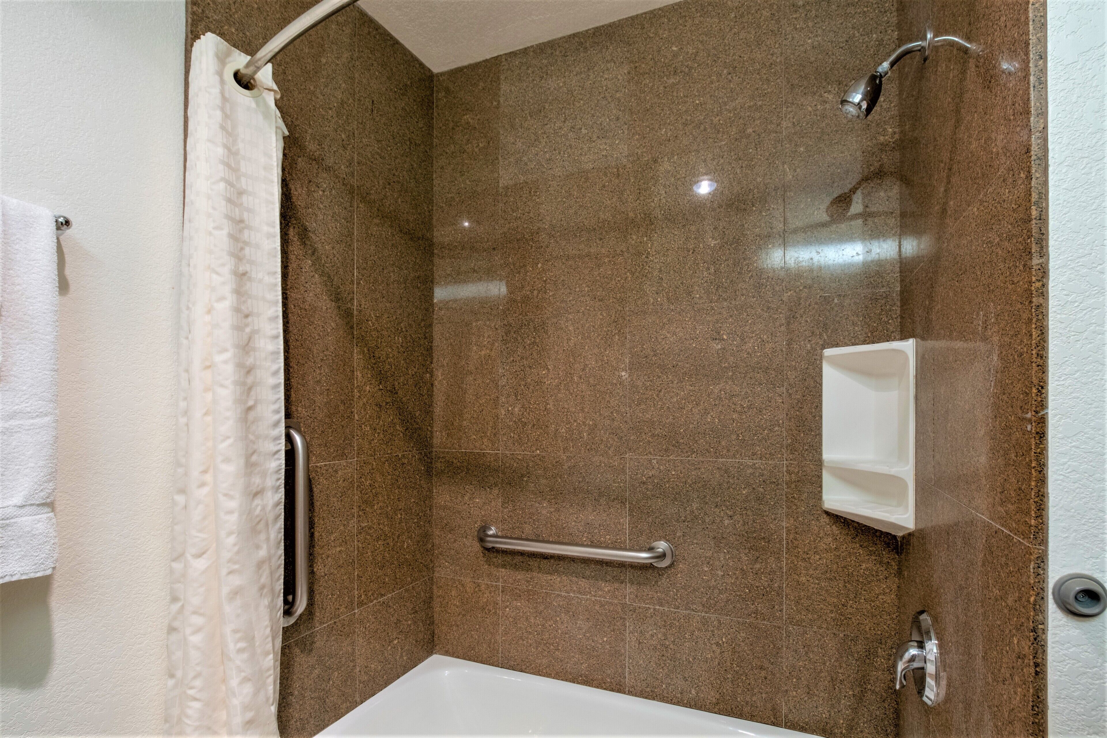 Un baño con ducha, barra de apoyo, perchero y jabonera.