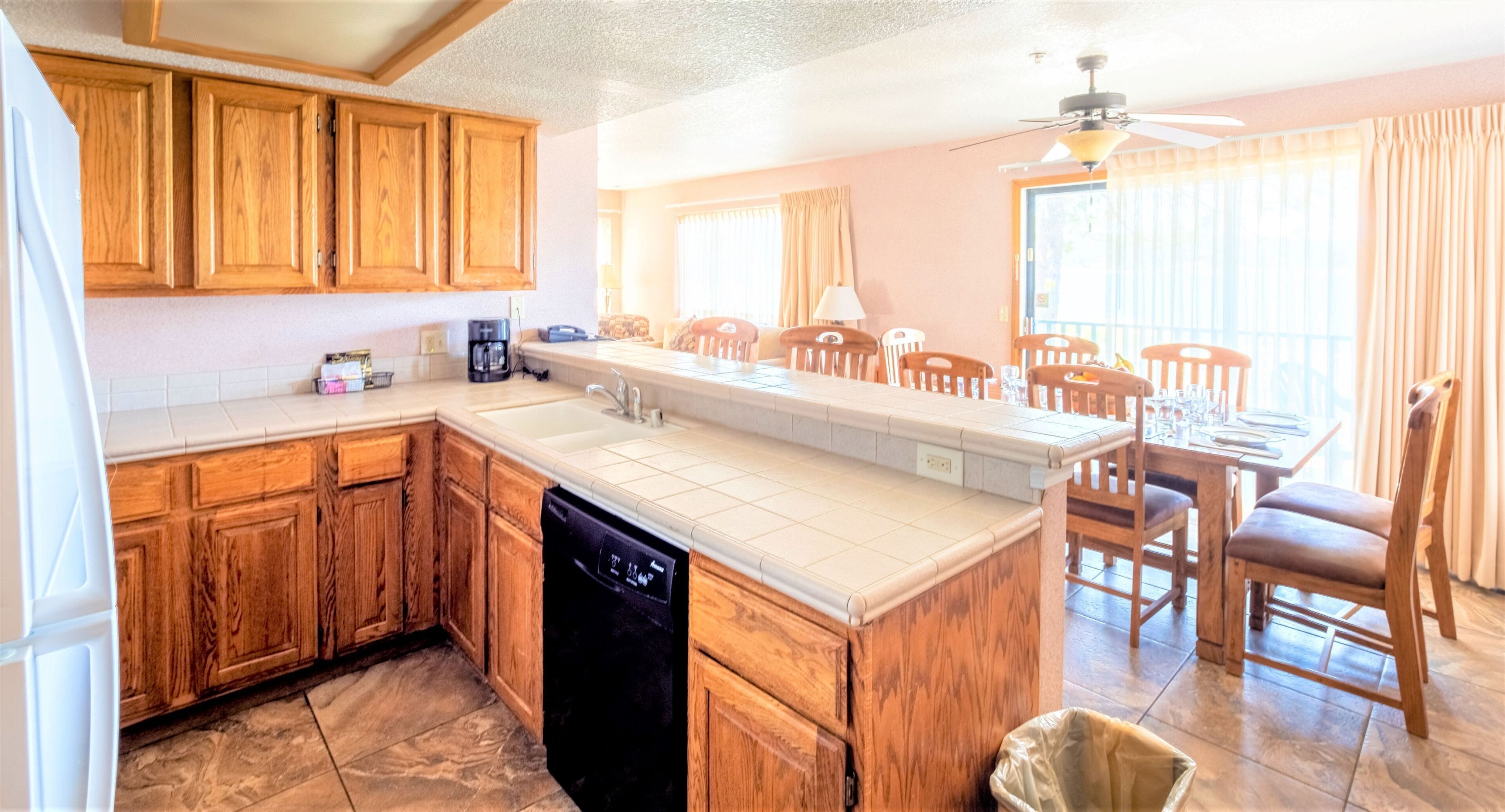 A kitchen with wooden cabinets, a dishwasher, a large island with a sink, and a dining area with wooden chairs.