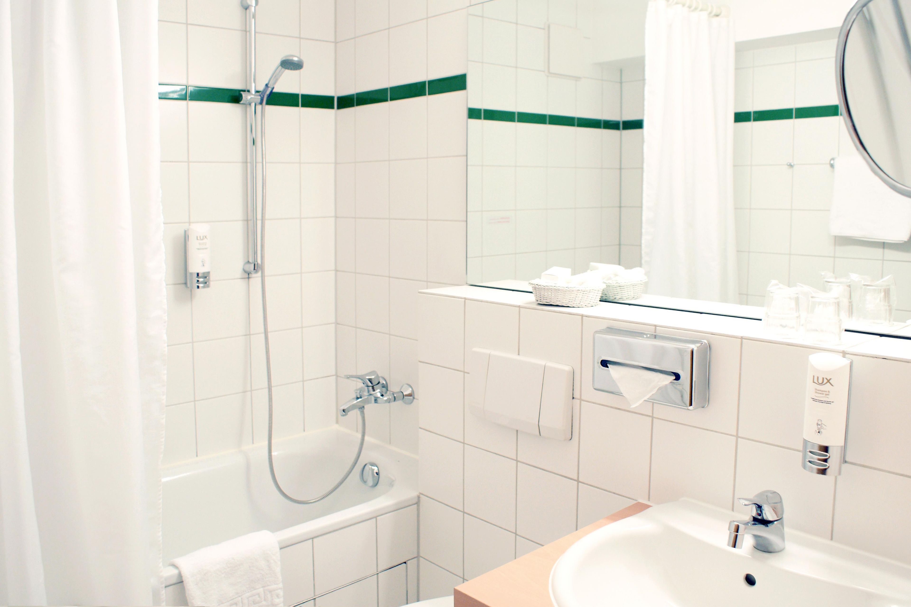 Un baño con ducha, lavabo, espejo y artículos de aseo en la encimera.