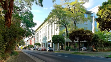 Une rue bordée d’immeubles à plusieurs étages, de voitures garées et d’arbres.