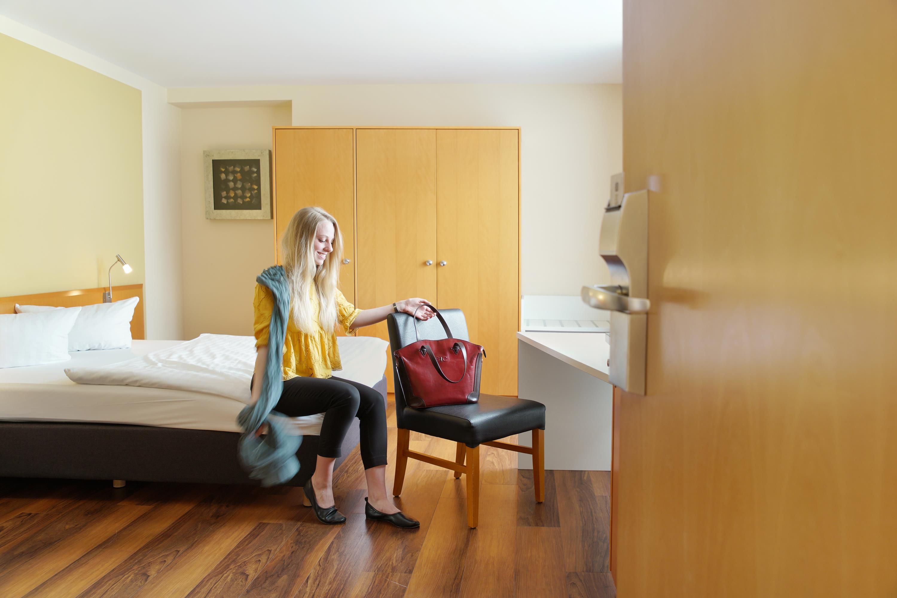 A hotel room with a bed, a desk, a chair, and a wardrobe.