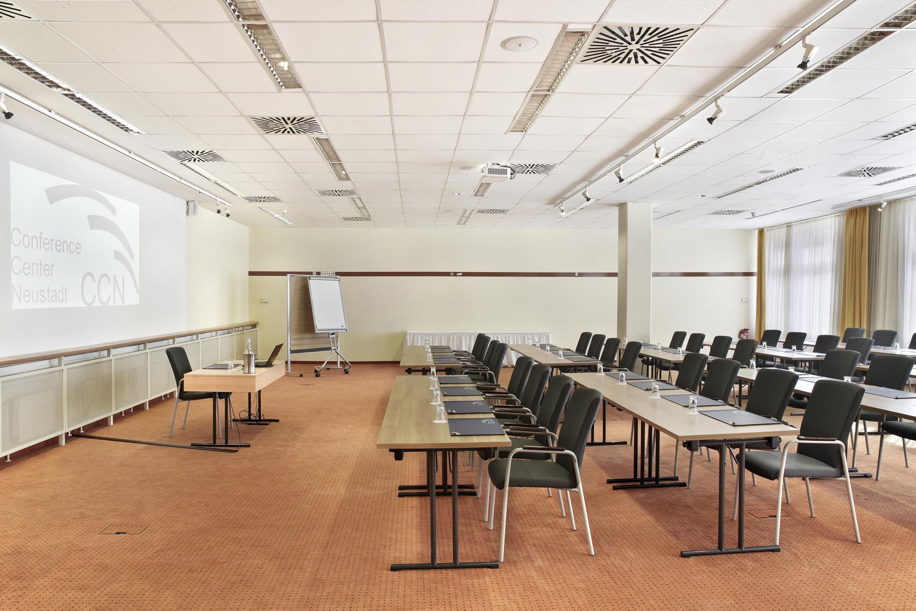 Un salón de conferencias con una larga mesa, sillas, una pantalla de proyector y una pizarra.