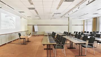 Un salón de conferencias con una larga mesa, sillas, una pantalla de proyector y una pizarra.