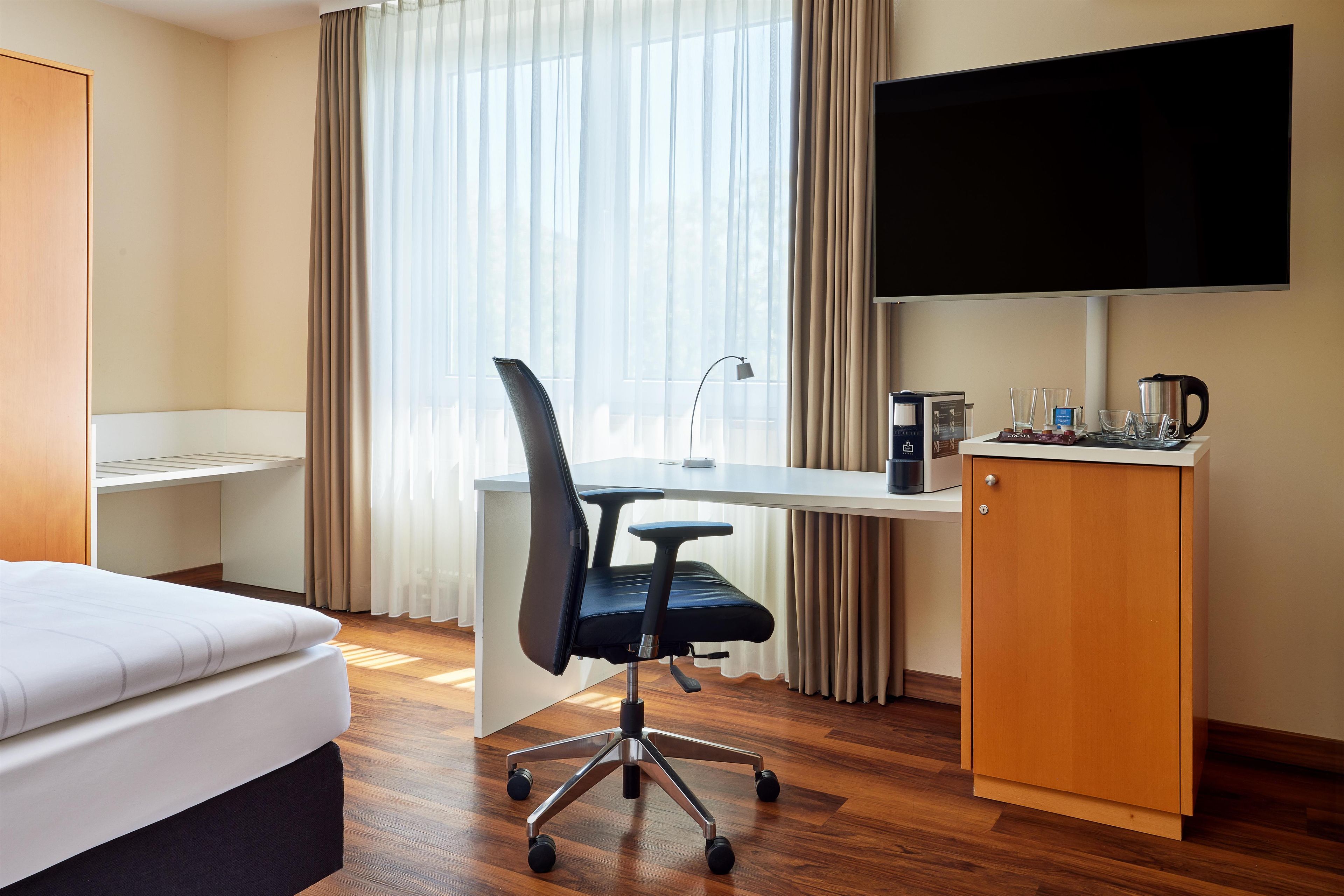 Una camera d'albergo con un letto, una scrivania, una sedia, una TV e un minibar.