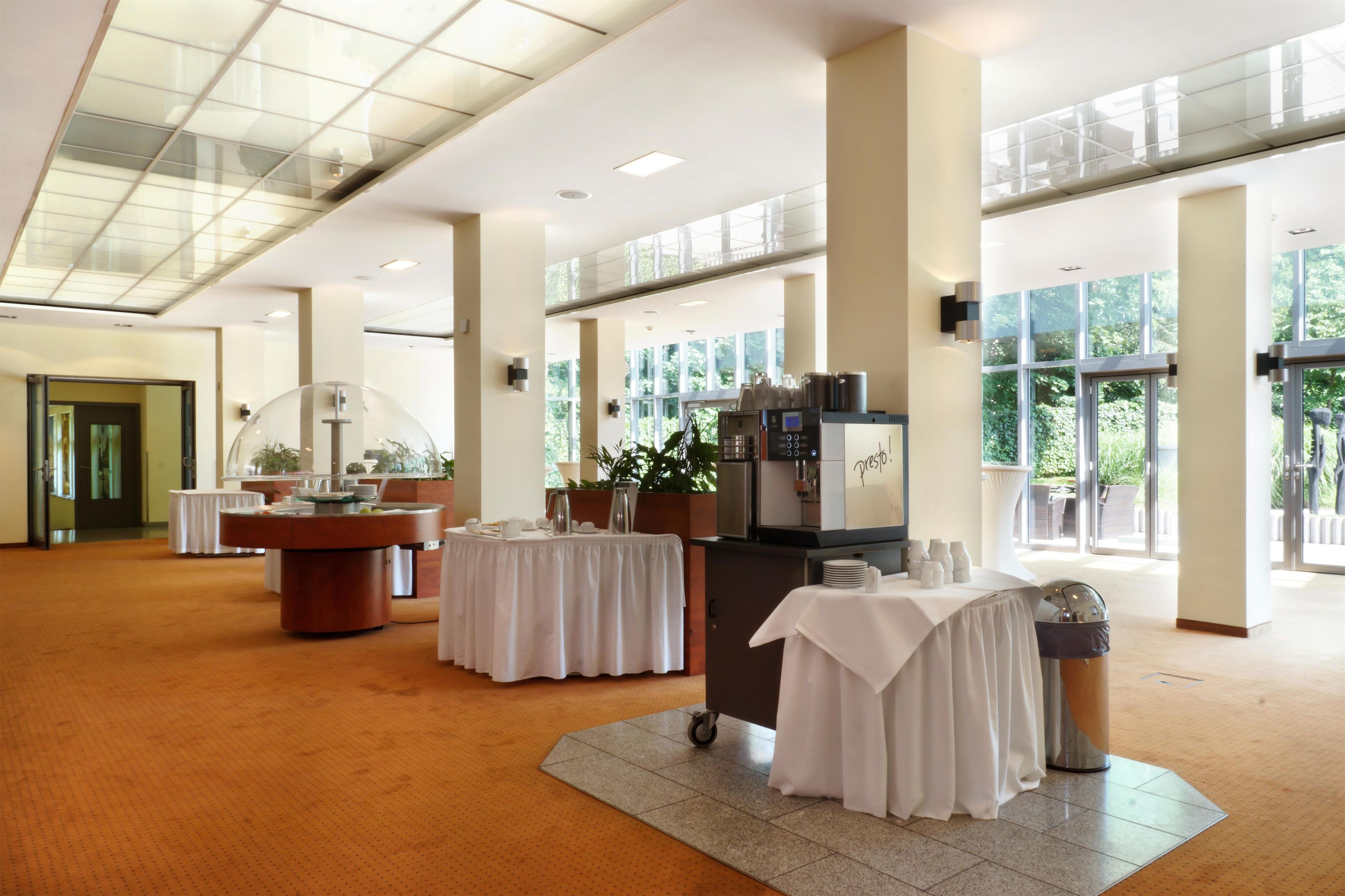 A spacious indoor area with a coffee station, tables with white tablecloths, and large windows allowing natural light.