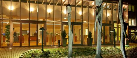 A hotel entrance with a glass facade, potted plants, and a paved walkway.