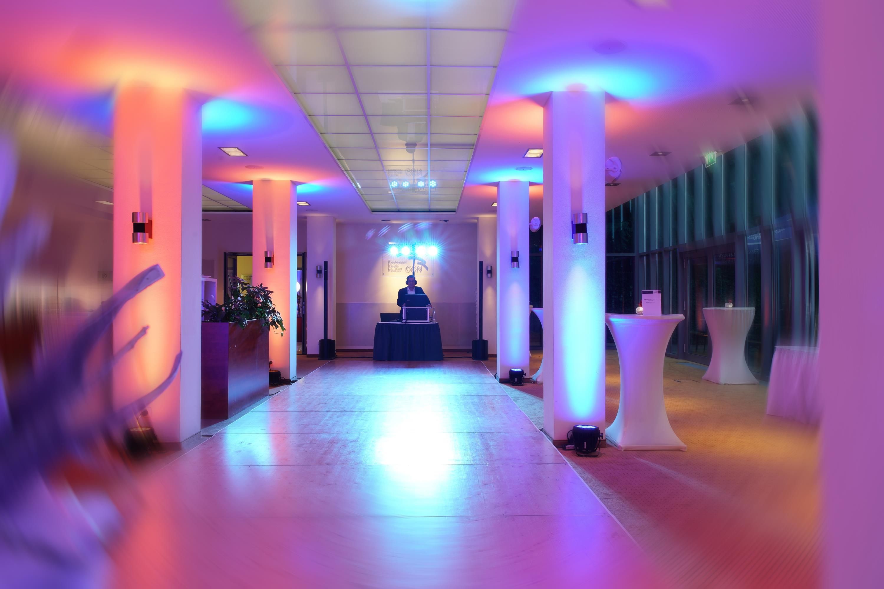Un pasillo de hotel con una mesa de recepción, un escenario con un atril y mesas con sillas.