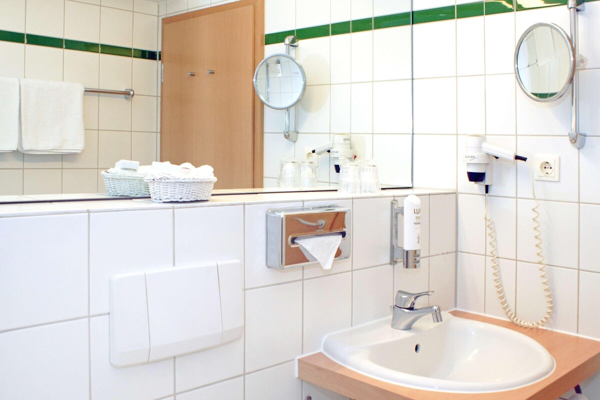 A bathroom with a sink, mirror, towel dispenser, and a hand dryer.