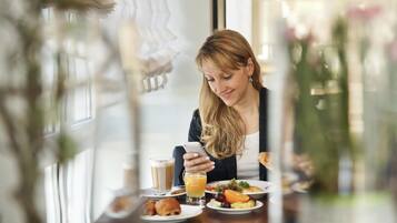 A person seated at a table with a meal, a glass of orange juice, and a smartphone.