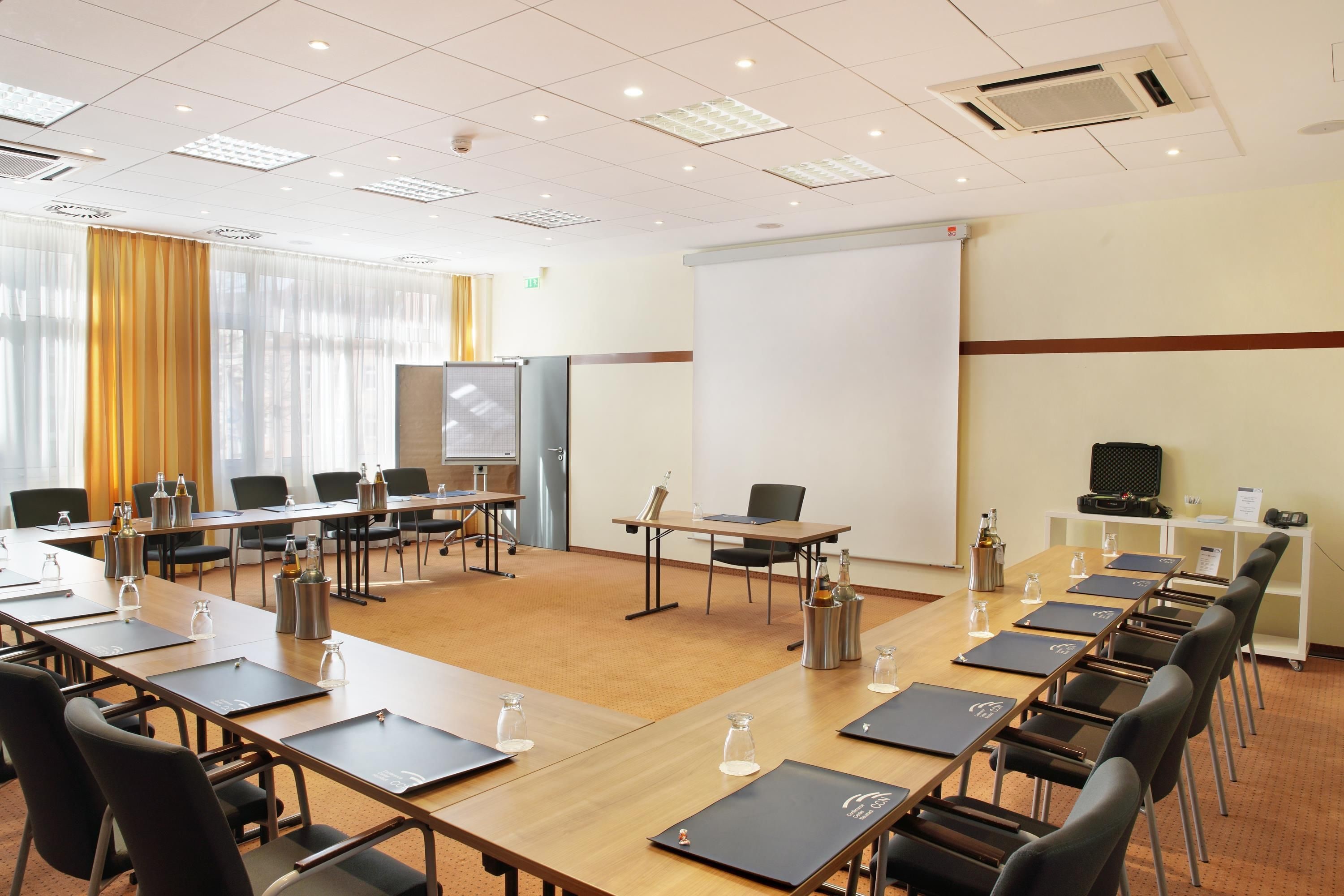 A conference room with a large white screen, multiple tables with chairs, and a projector.
