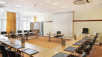A conference room with a large white screen, multiple tables with chairs, and a projector.