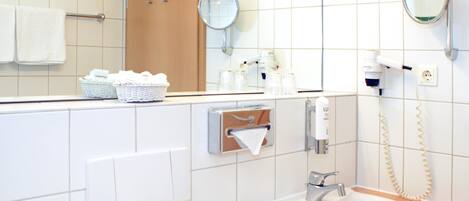 Un baño con lavamanos, espejo, dispensador de toallas y un secador de pelo en la pared.