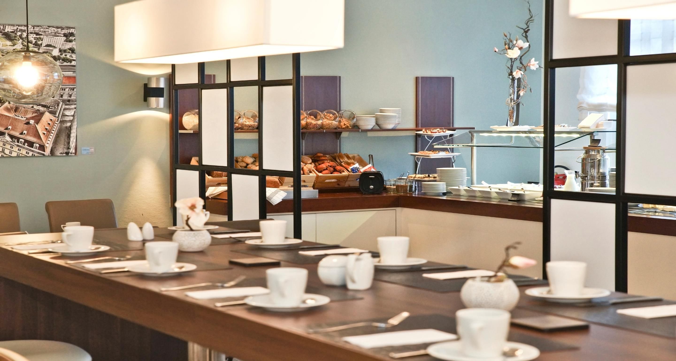 A conference room with a long table set for a meeting, a cityscape artwork on the wall, and a buffet area in the background.