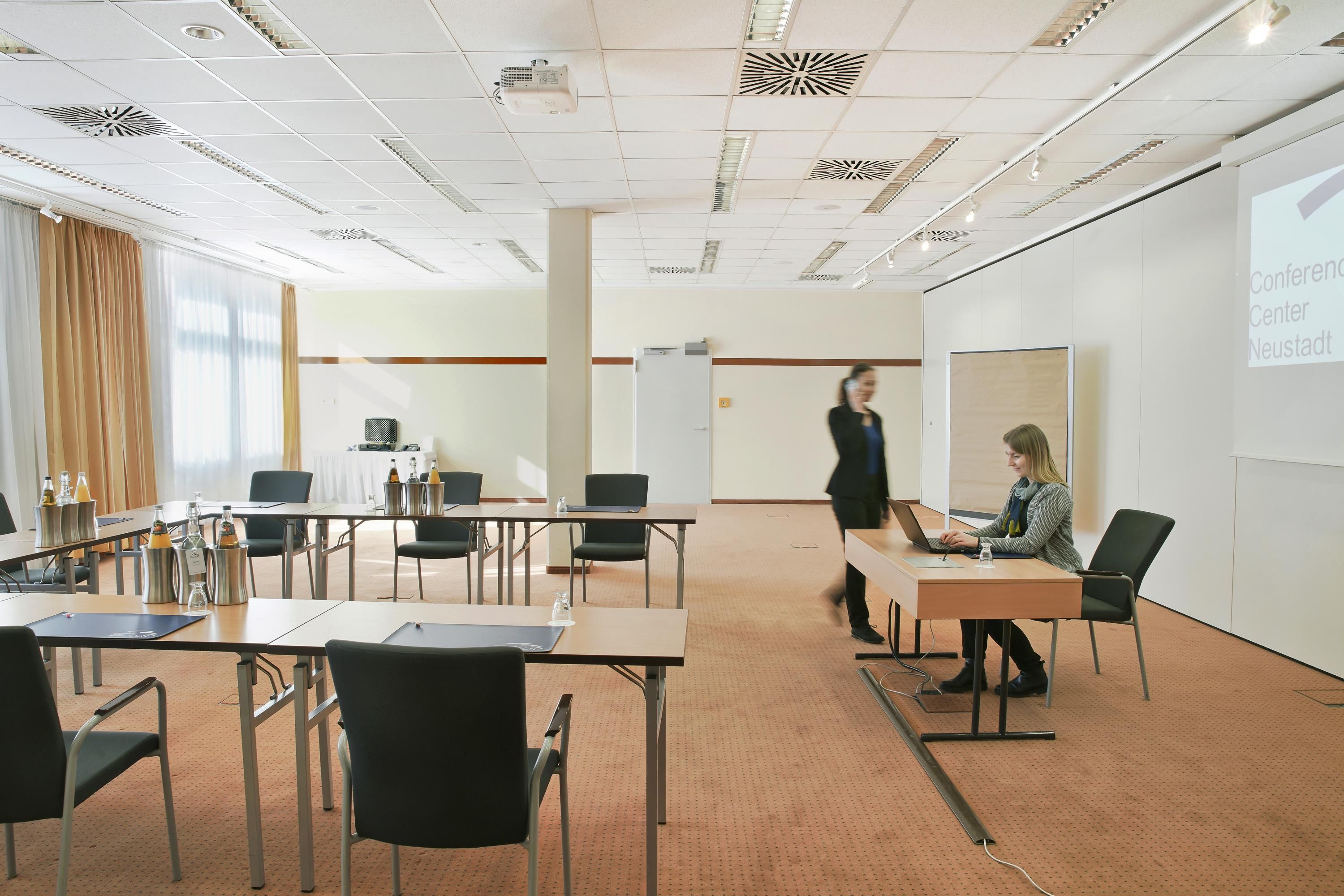 A conference room with tables, chairs, a projector screen, and a presentation in progress.