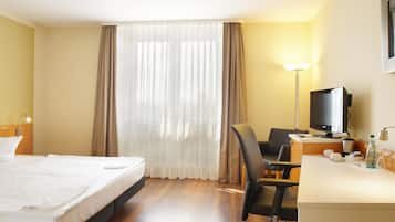 A hotel room with a bed, a desk with a computer, a chair, a television, and a window with curtains.