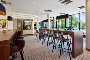 A modern bar area with a Starbucks, bar stools, and large windows offering a view of the outdoors. - Best Western Macrander Hotel Dresden (Dresden)