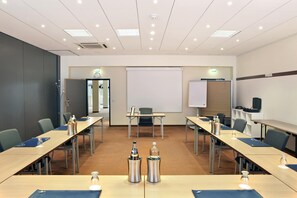 Una sala de conferencias con una pizarra grande, una pantalla de proyector y varias mesas con sillas.
