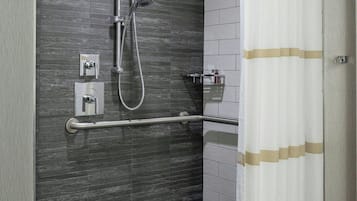 A modern bathroom with a shower, grab bar, and a towel rack.