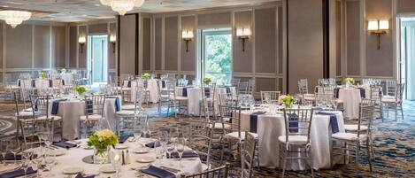 Un salón de banquetes con mesas redondas, manteles blancos y sillas de plata.