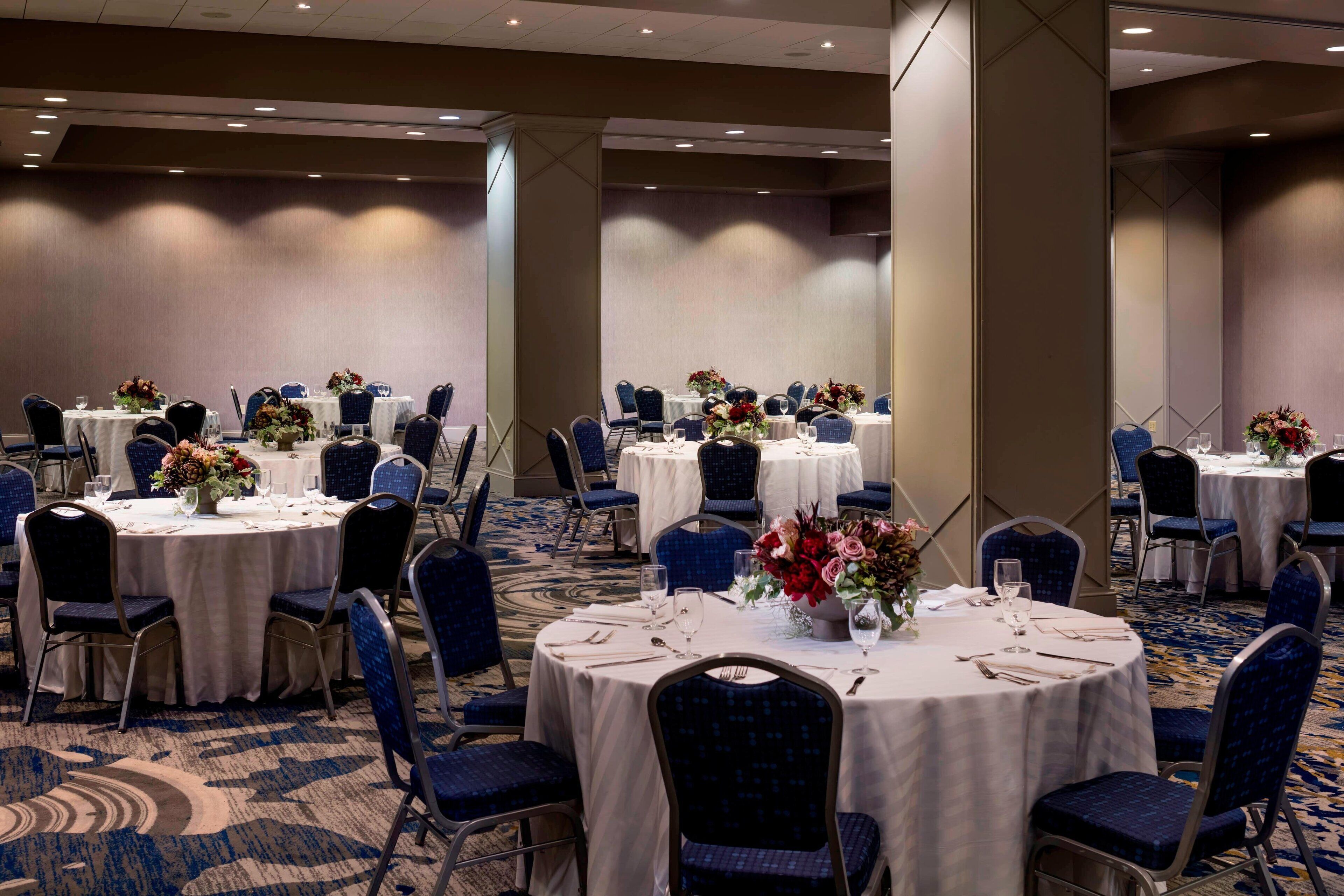 Un salón de conferencias con mesas redondas, sillas azules y centros de mesa con flores.