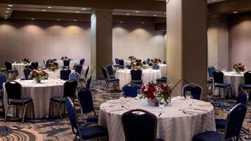 Un salón de conferencias con mesas redondas, sillas azules y centros de mesa con flores.