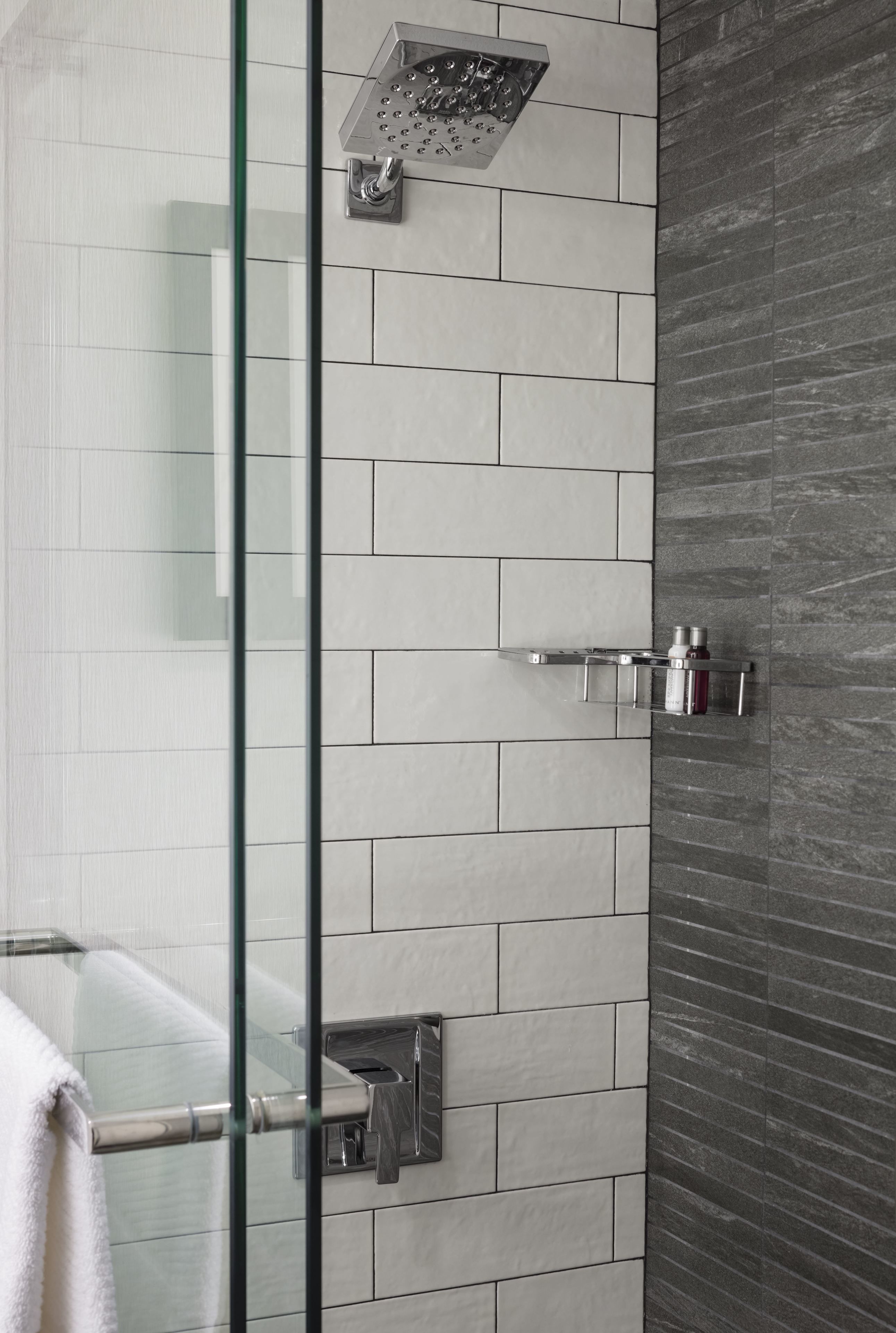 Une salle de bain moderne avec une douche à parois de verre, un mur recouvert de carreaux blancs et un mur d’accent en pierre sombre.