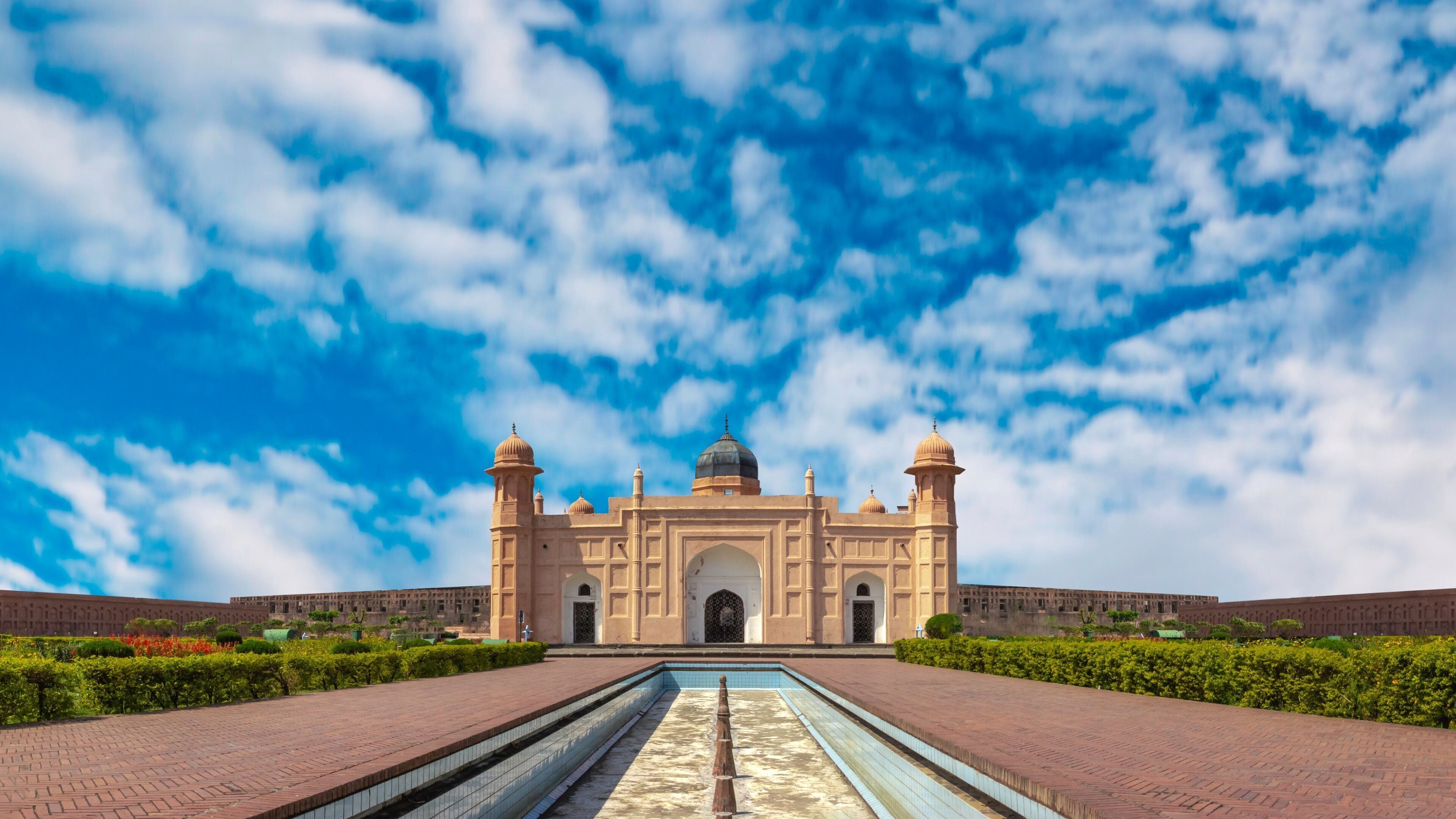 A large, historic building with a central dome and two towers, surrounded by a symmetrical garden and a long reflecting pool.