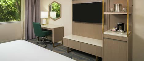 Habitación de hotel con cama, escritorio y silla, televisión, cafetera y estante con vasos.