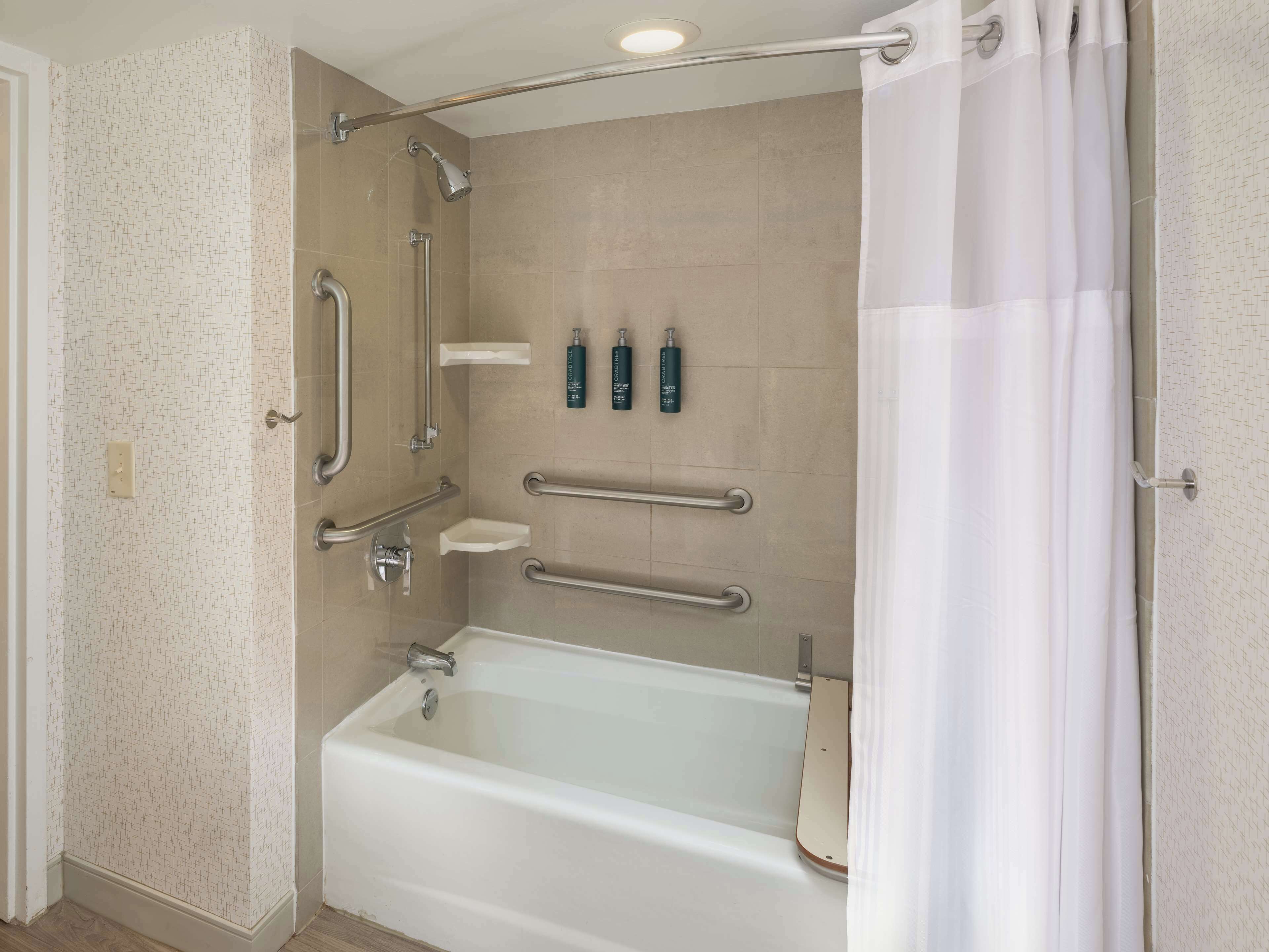 A modern bathroom with a bathtub, grab bars, a showerhead, and a toilet.