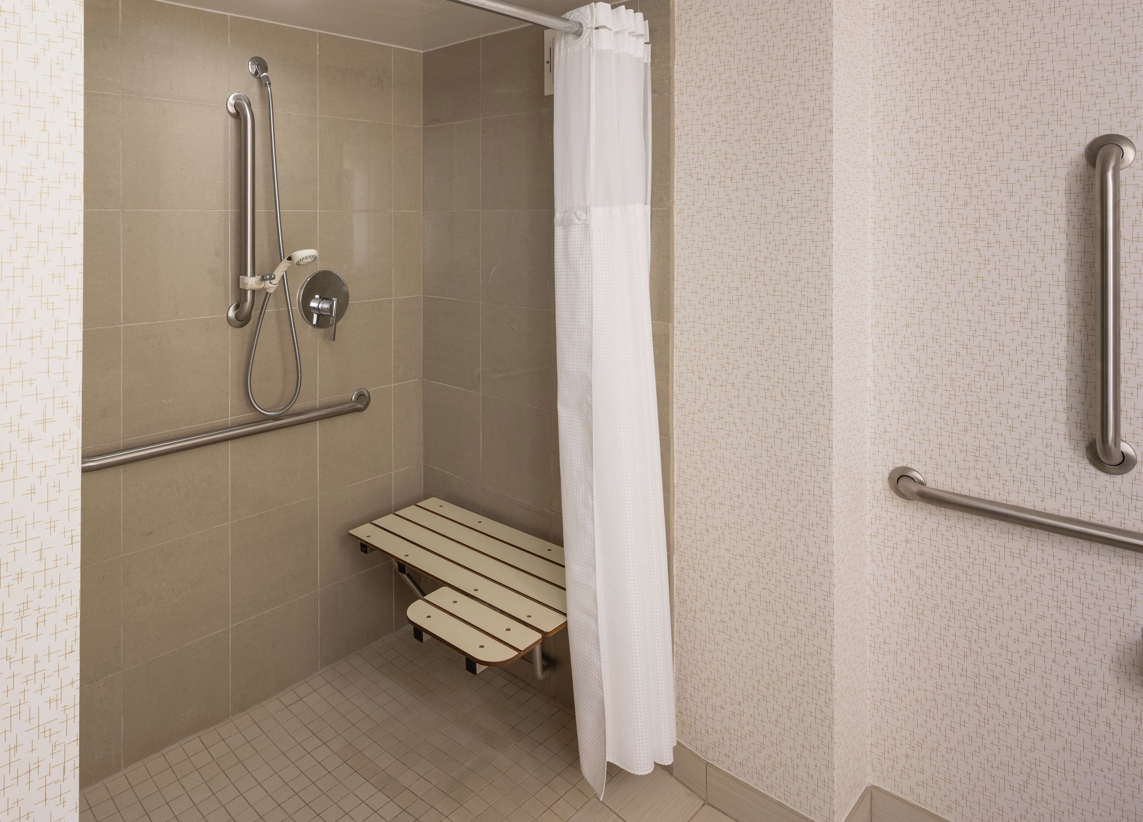 A shower area with a bench, grab bars, and a showerhead.