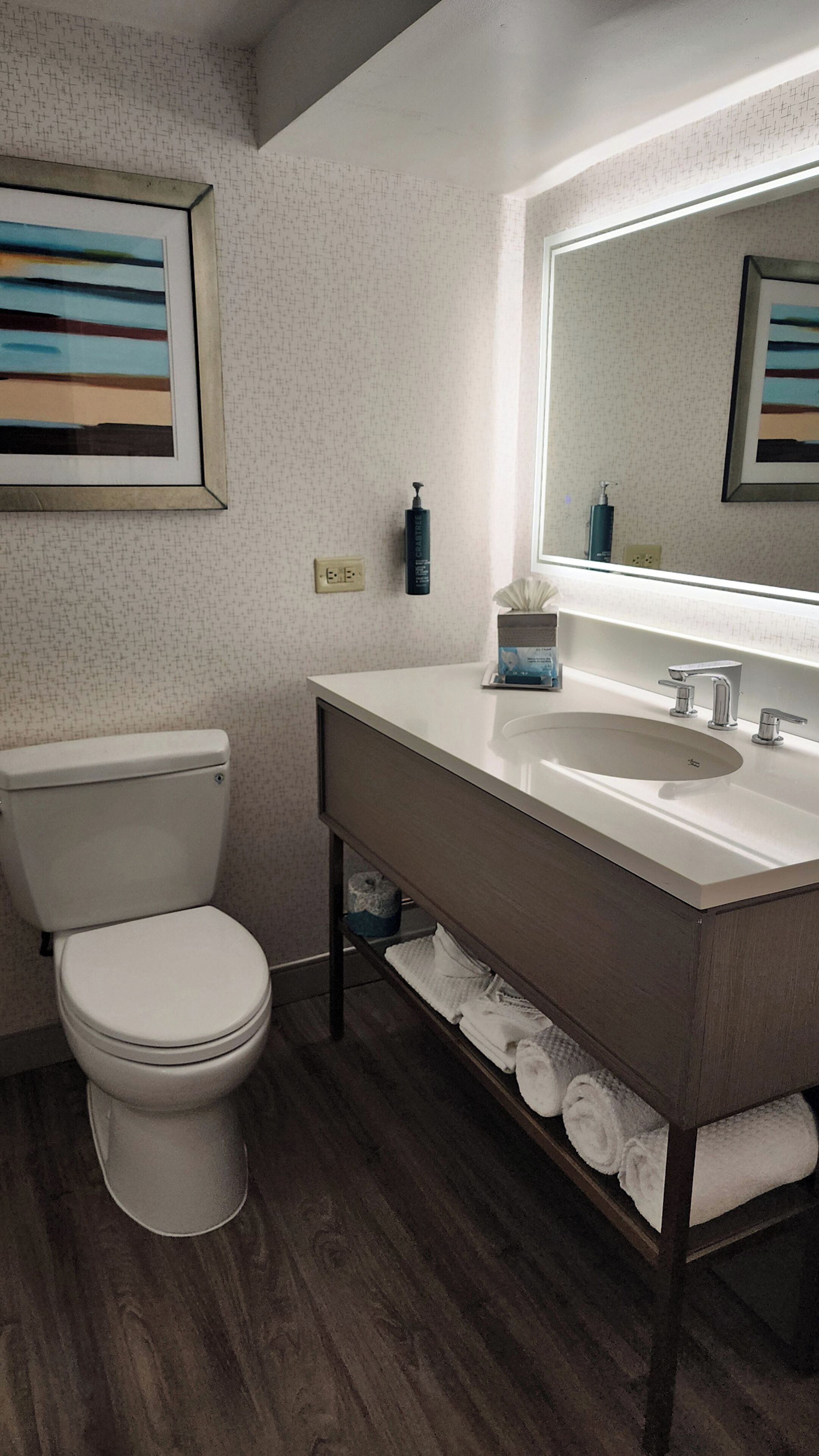 Une salle de bain moderne avec des toilettes, un lavabo et un miroir. Il y a des serviettes sur le sol et un distributeur de savon sur le lavabo.