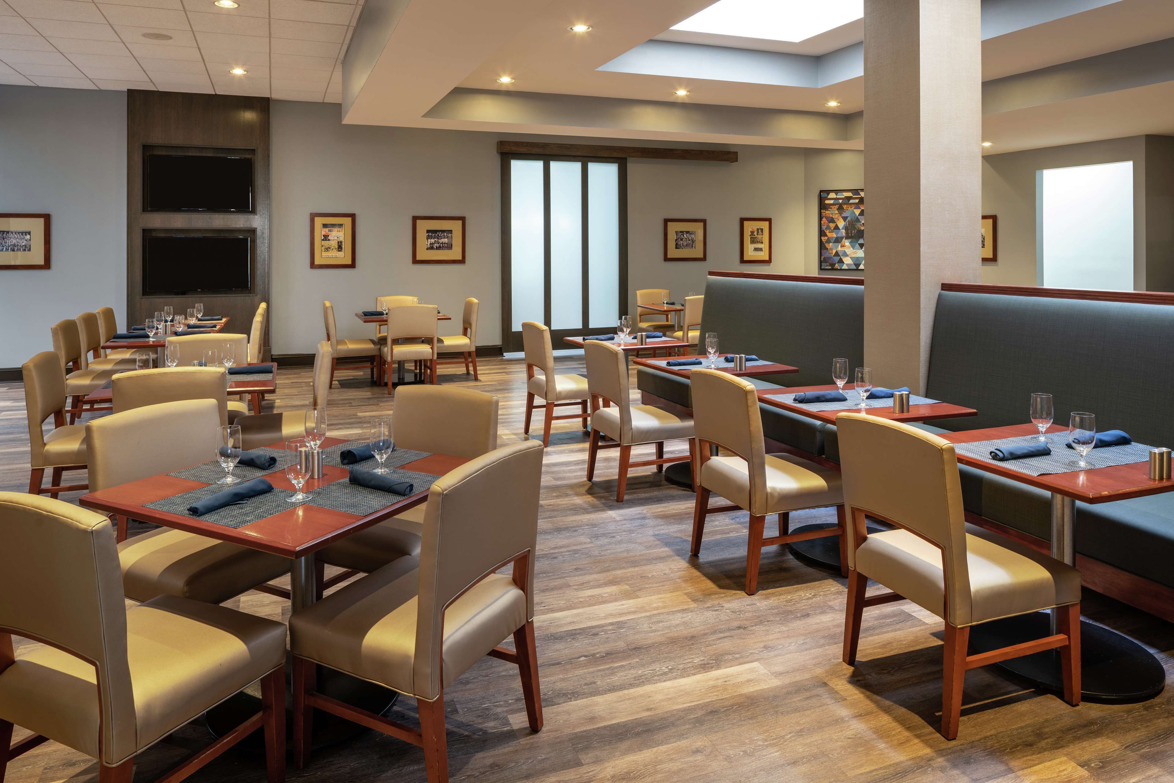 A modern dining area with multiple tables and booths, wooden flooring, and framed artwork on the walls.